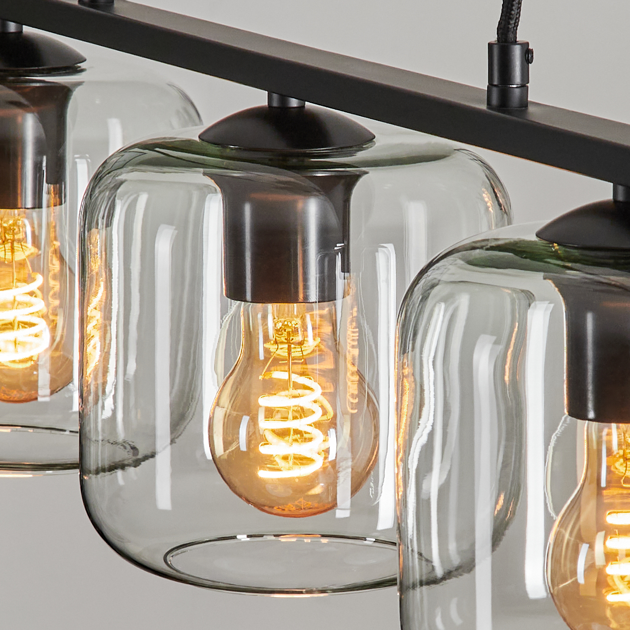 Nahaufnahme einer modernen Leuchte mit drei Glasschirmen. Jeder Schirm hat eine warme, leuchtende Glühbirne im Inneren und einen schwarzen Metallrahmen.