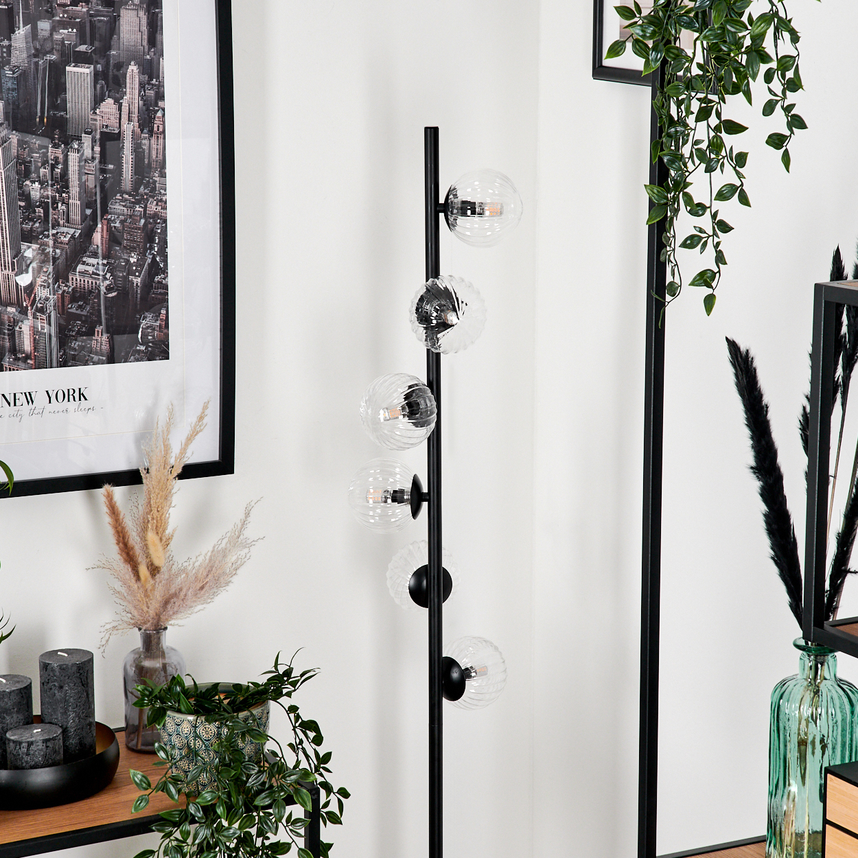 Ein modernes Wohnzimmer mit einer schwarzen Stehlampe mit Glaskugelleuchten, einem New York City-Druck und verschiedenen Pflanzen.