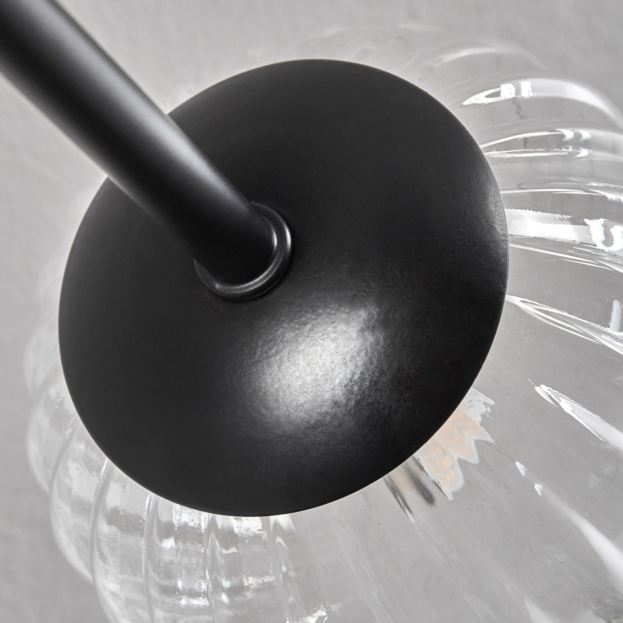 Nahaufnahme einer schwarzen Metall-Lampenfassung. Ein runder Sockel bedeckt einen transparenten, strukturierten Glasschirm. Der Lampenarm erstreckt sich vom Sockel.
