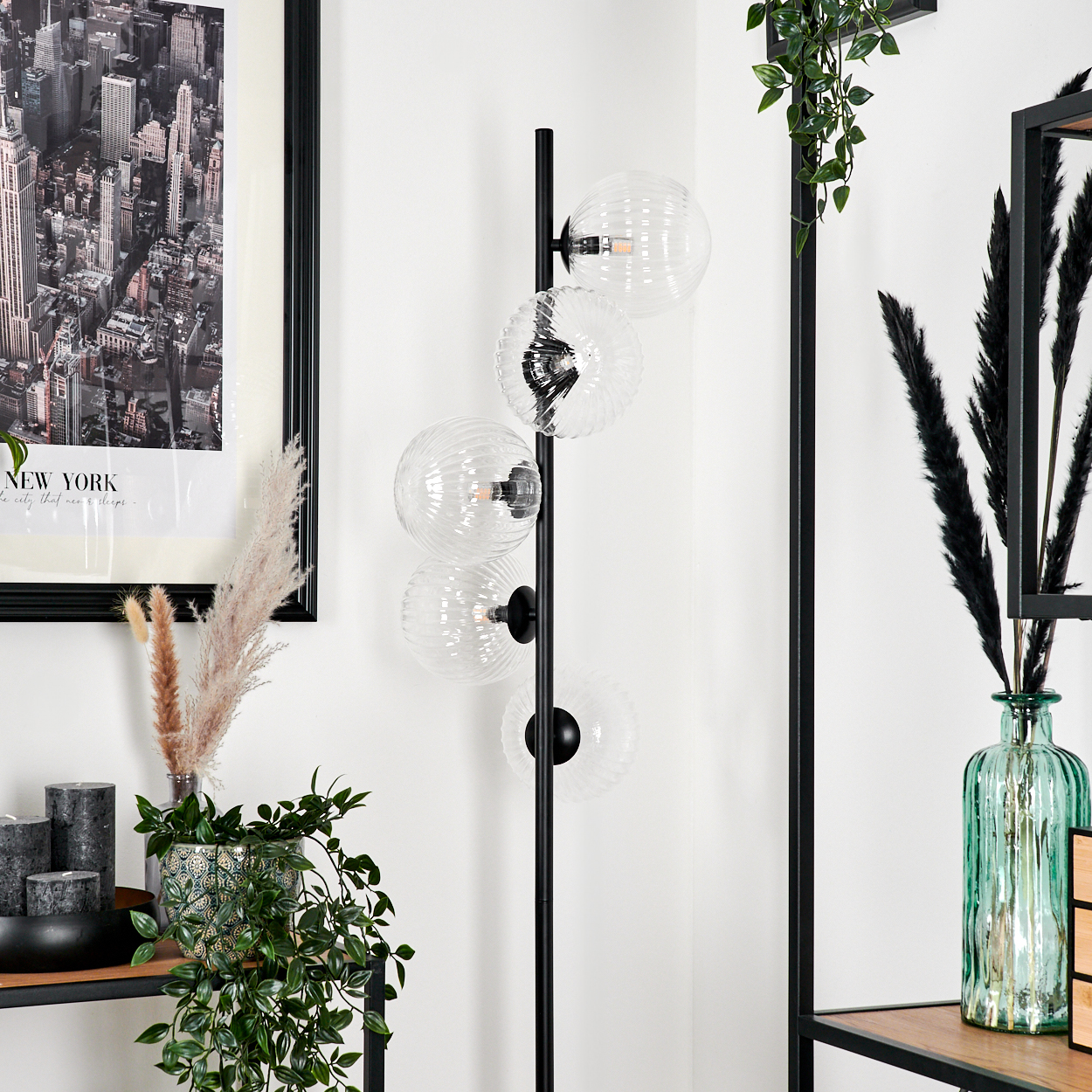 Ein modernes Interieur mit einer schwarzen Stehlampe mit Glaskugeln, einem gerahmten New York-Bild und dekorativen Pflanzen.