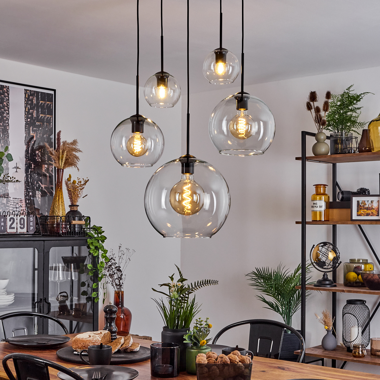 Esszimmer mit Holztisch, schwarzen Stühlen, Glaskugel-Pendelleuchten und einem Regal mit Dekoration.
