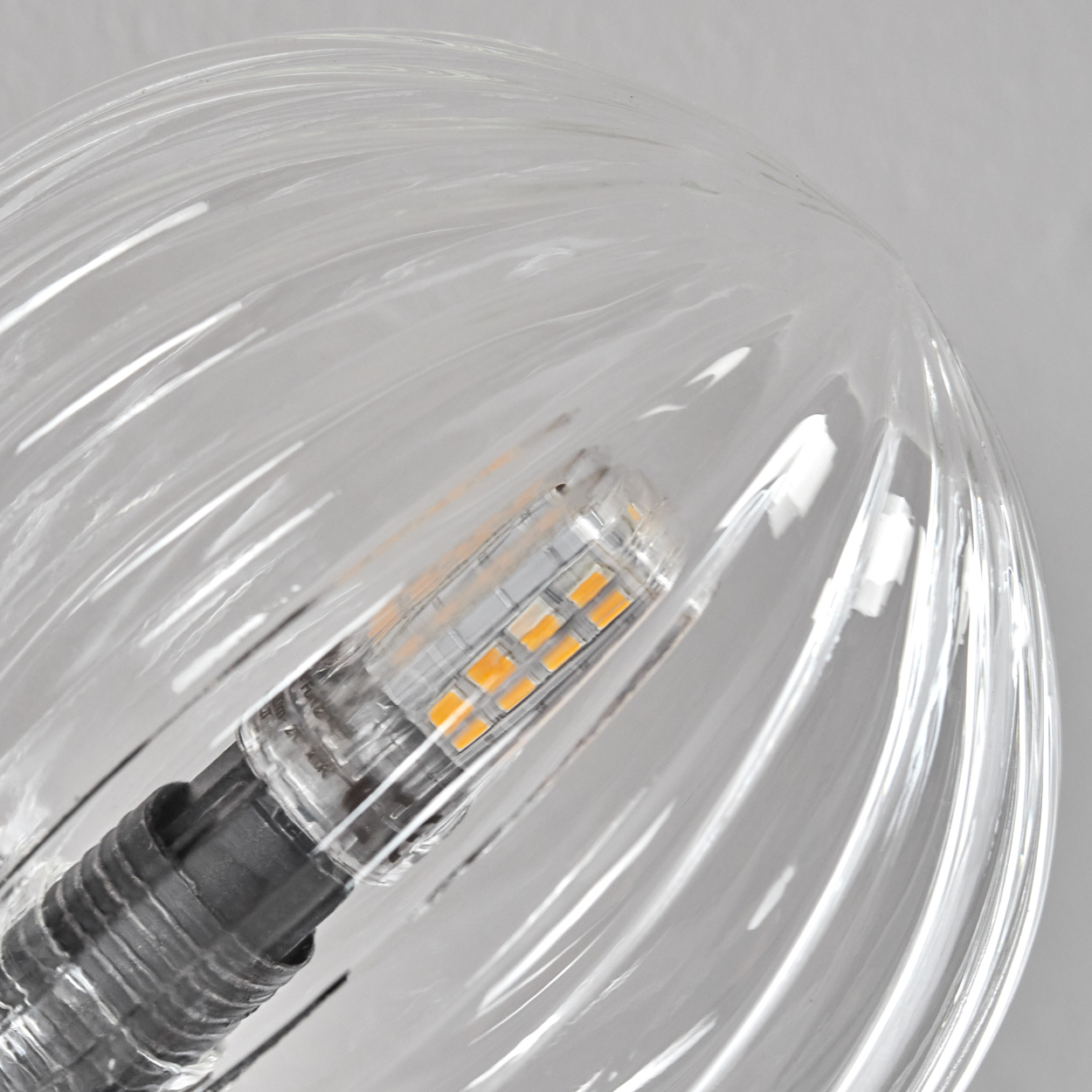 Nahaufnahme einer klaren, geriffelten Glasglühbirne. Im Inneren ist eine kleine LED-Leuchte mit orangefarbenen und weißen Segmenten zu sehen.