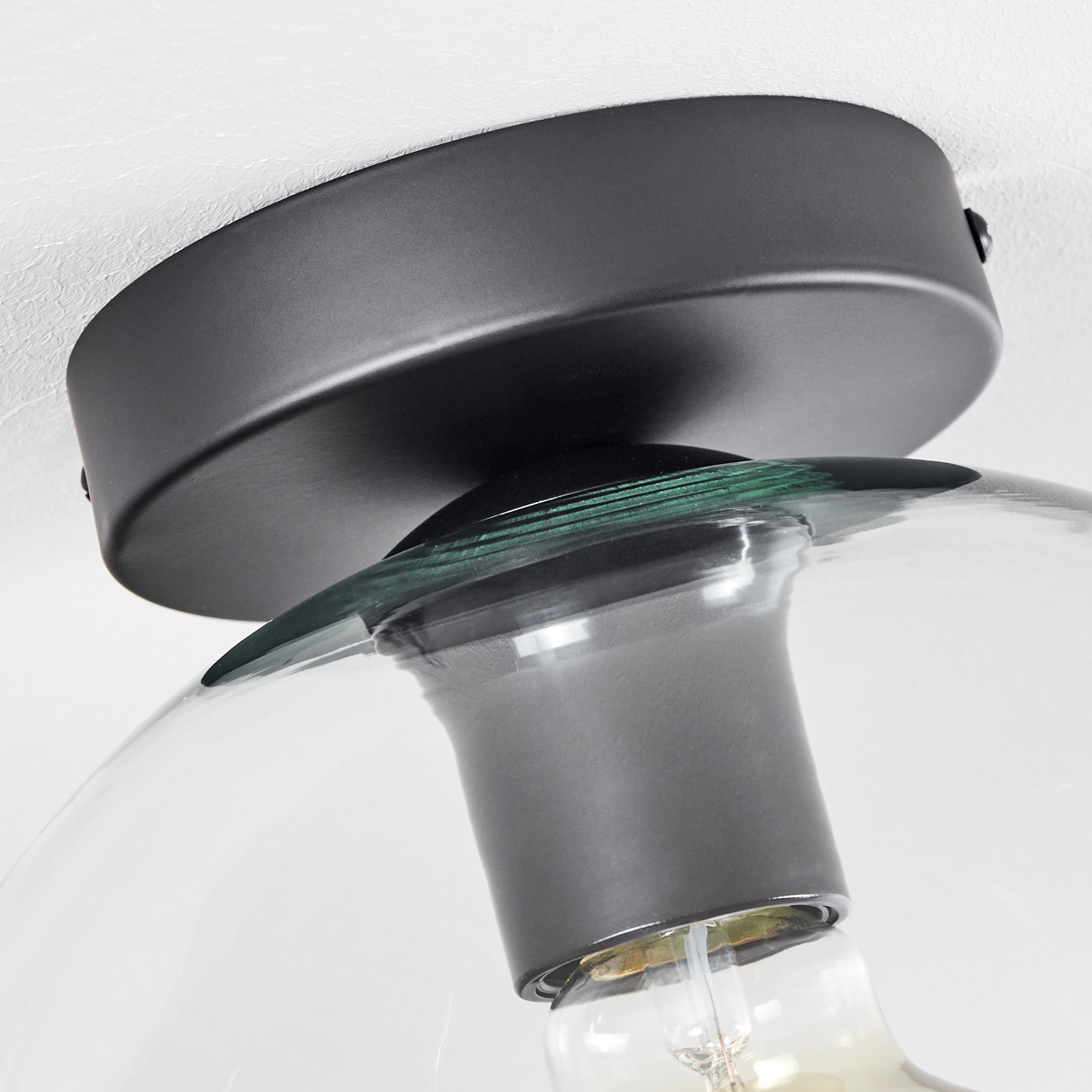 Nahaufnahme einer modernen Deckenlampe mit schwarzem Sockel und klarem Glasschirm, der die Glühbirne zeigt.