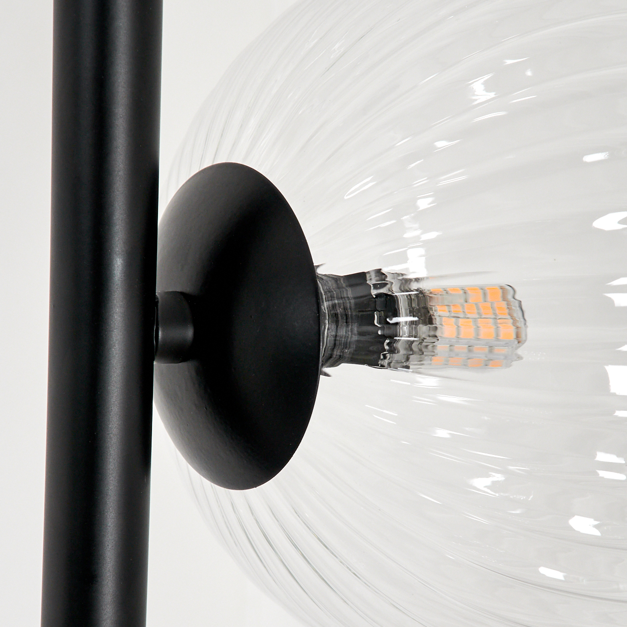 Nahaufnahme einer schwarzen Lampe mit einer klaren, gerippten Glaskugel. Die Lampe hat einen schwarzen Stiel und eine sichtbare Glühbirne.