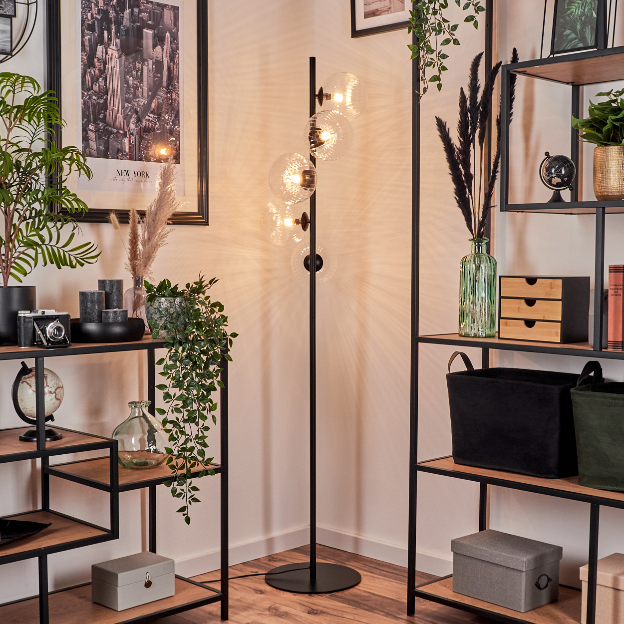 Eine Zimmerecke mit Stehlampe, Bücherregalen, Pflanzen und einem New York City Poster.