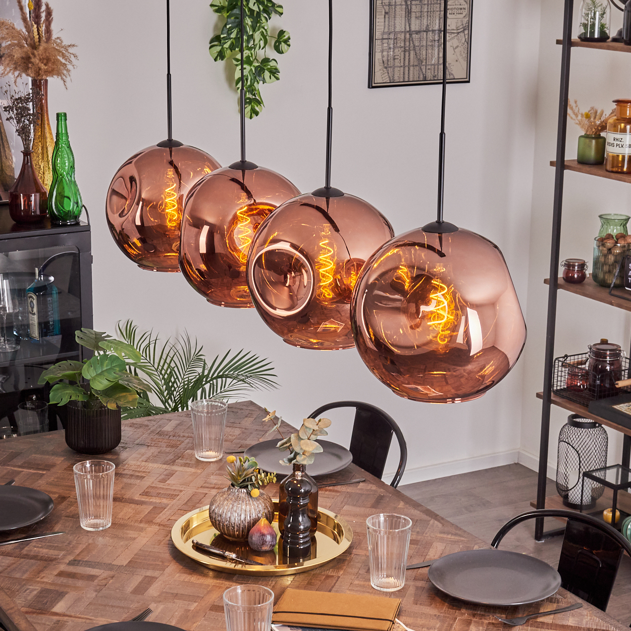 Esszimmer mit kupferfarbenen Pendelleuchten. Holztisch mit Tellern, Gläsern und einer Tablett mit Dekorationen. Regale mit Gläsern.