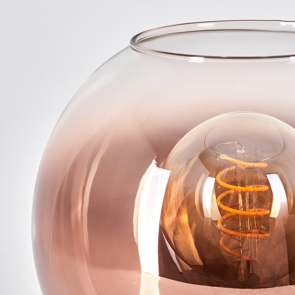 Eine dekorative Lampe mit kupferfarbenem Glasschirm. Im Inneren leuchtet eine Glühbirne mit Spiralfaden vor weißem Hintergrund.