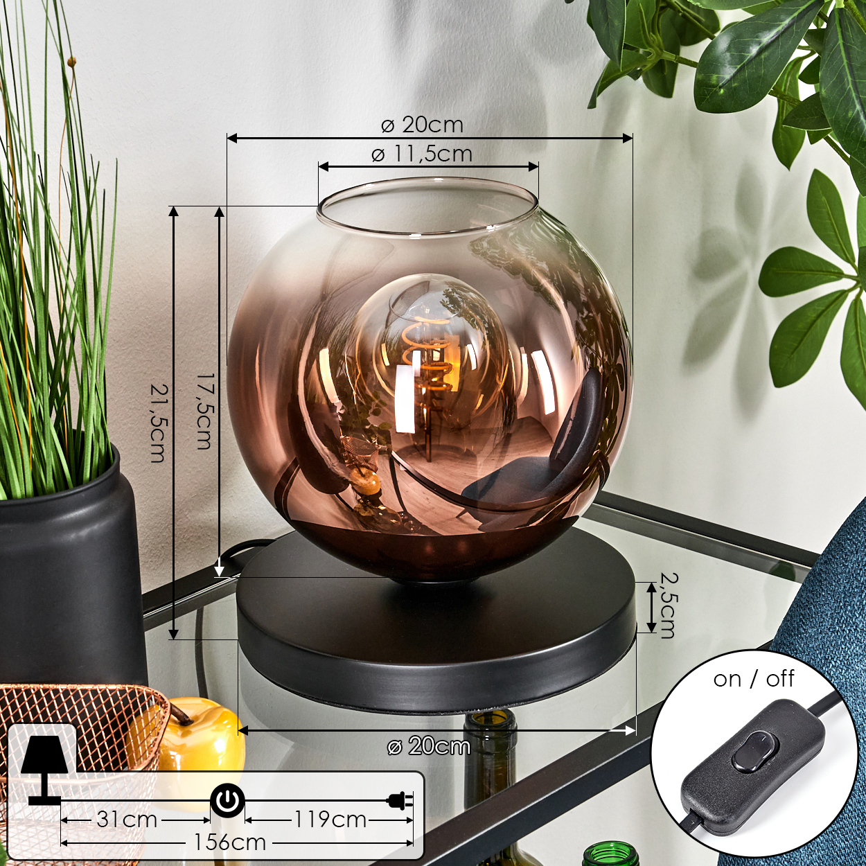 Dekorative Lampe mit kupferfarbenem Glasschirm auf schwarzem Sockel. Links ein schwarzer Topf mit grünem Gras.