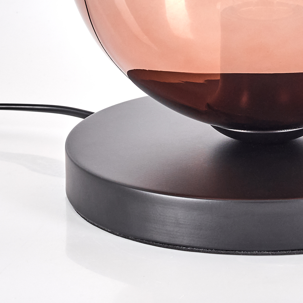 Nahaufnahme einer Lampe. Sie hat eine kupferfarbene Oberseite und einen schwarzen Sockel. Ein schwarzes Kabel ist sichtbar.