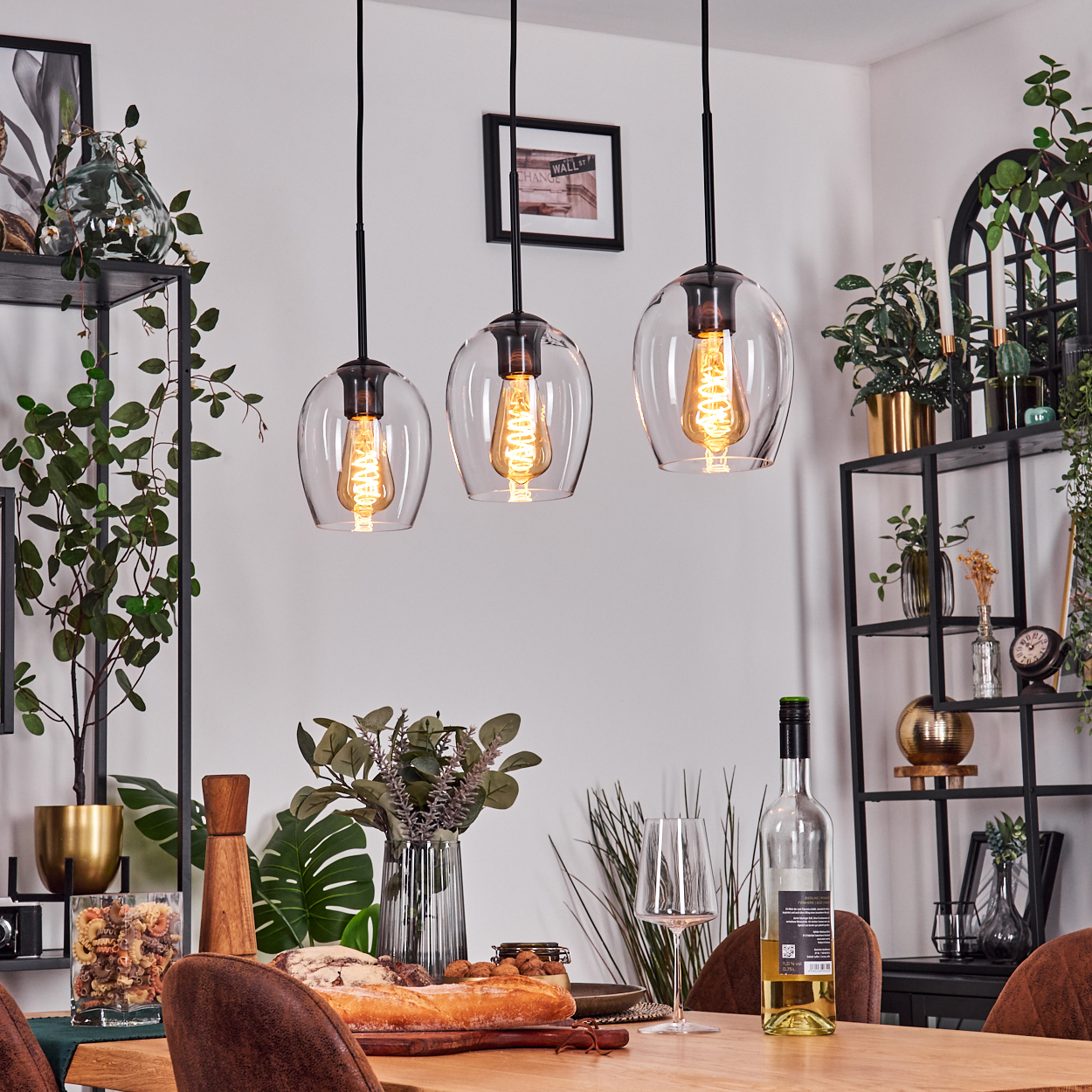 Esszimmer mit Hängelampen, Tisch mit Essen und Wein. Regale mit Pflanzen im Hintergrund.