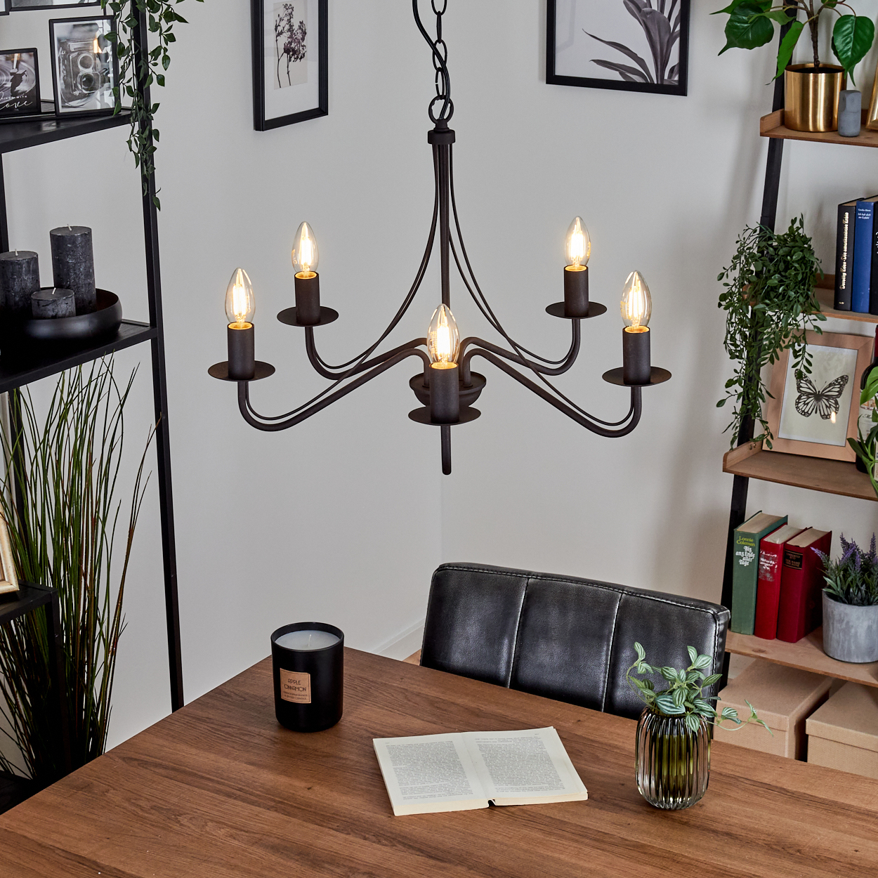Esszimmer mit Holztisch, Kronleuchter, schwarzer Kerze, offenem Buch, Vase und schwarzem Lederstuhl.