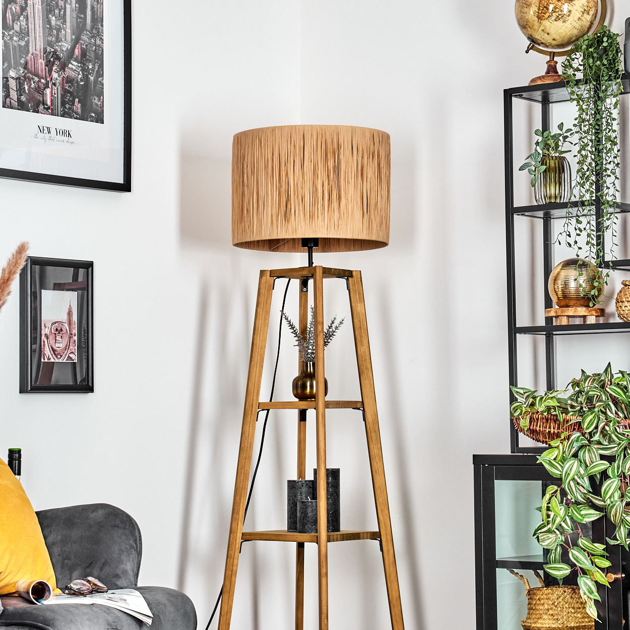 Eine Zimmerecke mit einer Holzlampe, einem schwarzen Regal mit Pflanzen und einem Globus sowie einem grauen Sessel mit gelbem Kissen.
