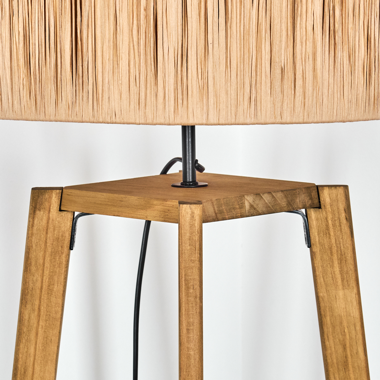 Nahaufnahme einer Stehlampe. Sie hat einen Holzsockel mit einem gewebten Lampenschirm. Ein schwarzes Kabel verbindet sich mit der Lampe.