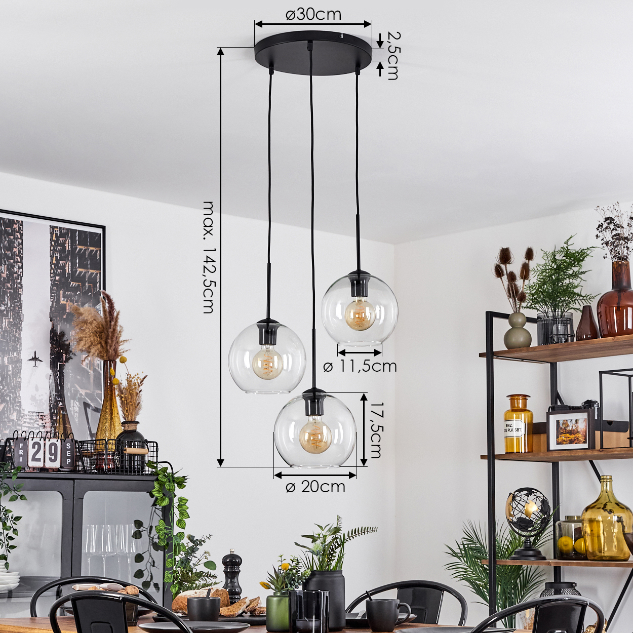 Dreifach-Pendelleuchte mit klaren Glaskugeln. Maße sind markiert. Esstisch mit Dekoration im Vordergrund, Regal mit Dekoration im Hintergrund.