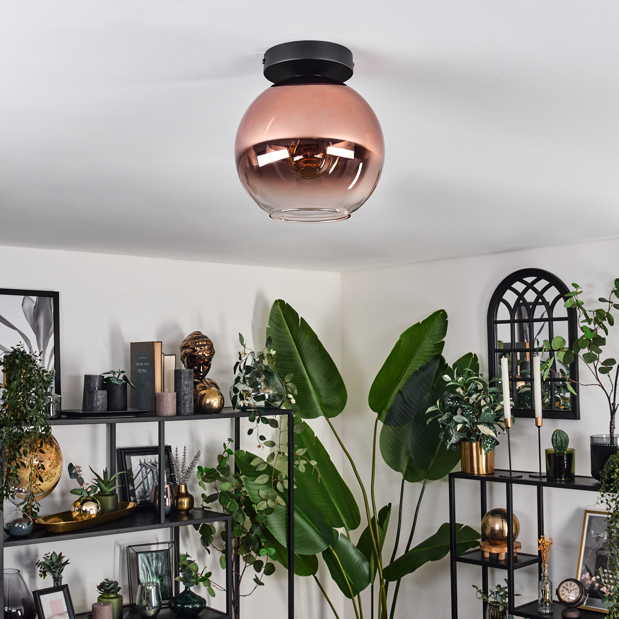 Ein modernes Wohnzimmer mit einer kupferfarbenen Deckenlampe, Regalen mit Pflanzen und Dekorationen und großen grünen Blättern.