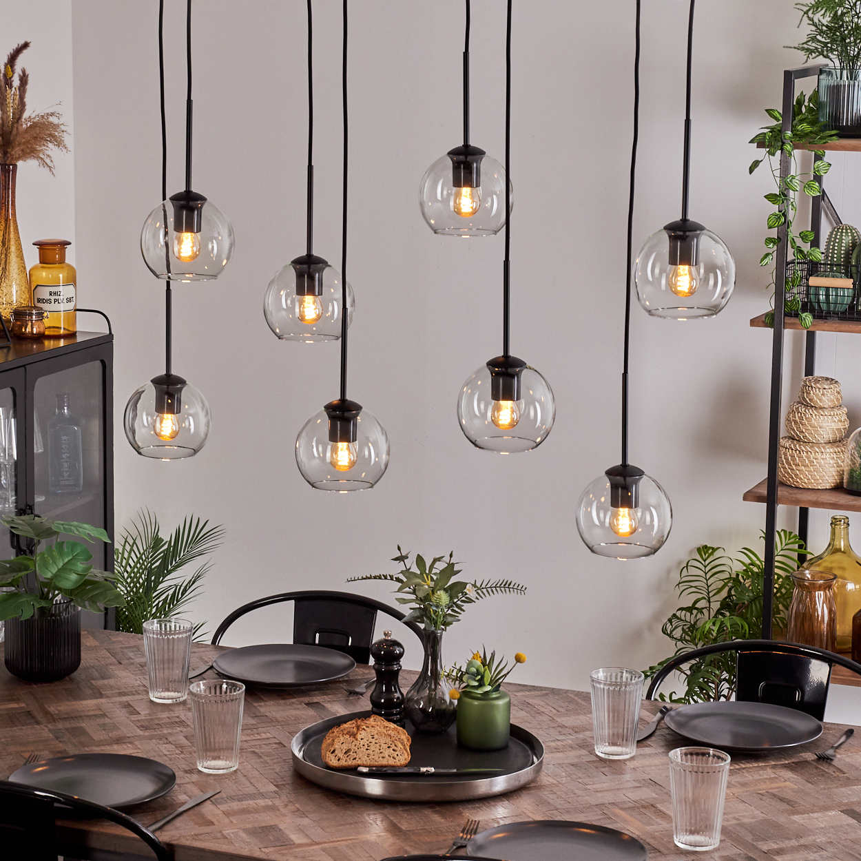 Esstisch mit acht Hängelampen. Tisch mit Tellern, Gläsern und Essen gedeckt. Pflanzen und Dekoration im Hintergrund.