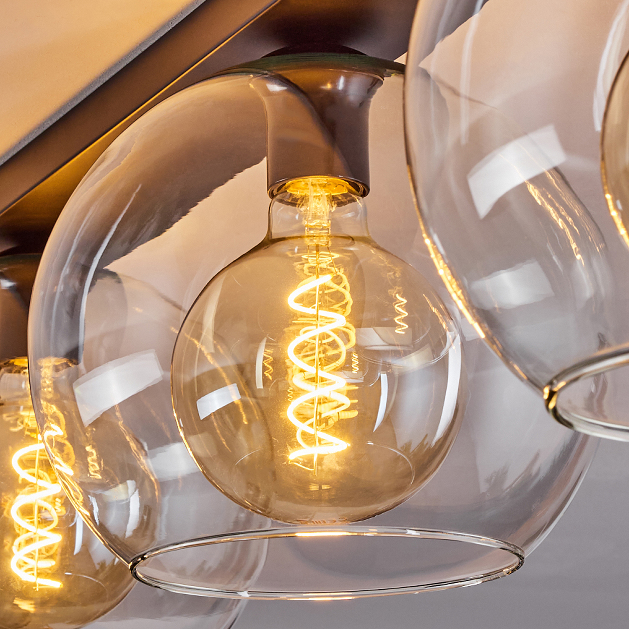 Nahaufnahme einer modernen Leuchte mit klaren Glaskugeln und leuchtenden Glühbirnen im Edison-Stil. Braune Leuchte und beige Wand.