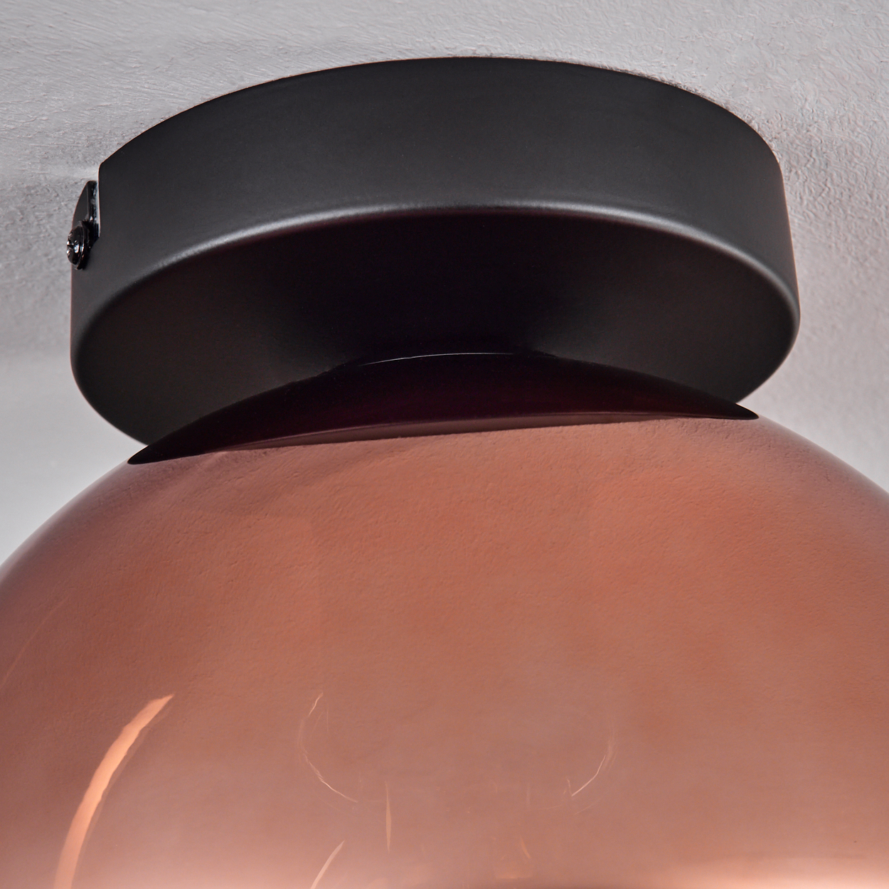 Nahaufnahme einer Deckenlampe. Sie hat einen schwarzen Deckel und einen kupferfarbenen, kuppelförmigen Schirm. Der Hintergrund ist eine weiße Decke.