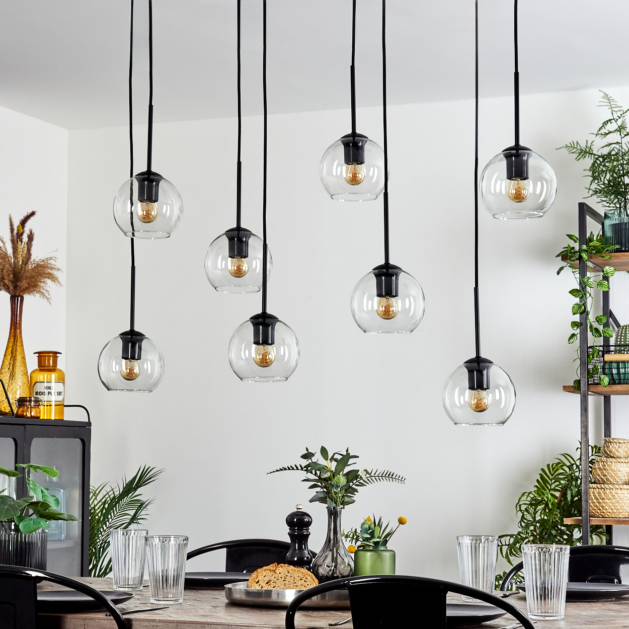 Esszimmer mit hängenden Kugelleuchten. Tisch mit Gläsern und Pflanzen. Ein Regal beherbergt Pflanzen und Dekoration.