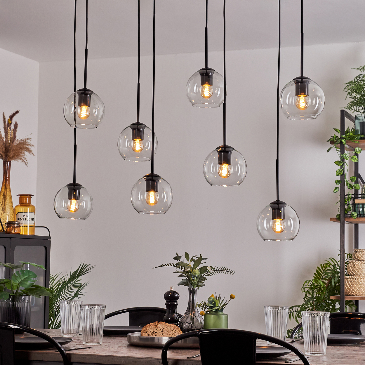 Esszimmer mit acht kugelförmigen Pendelleuchten, Tisch mit Gläsern und Essen, sowie dekorativen Pflanzen.
