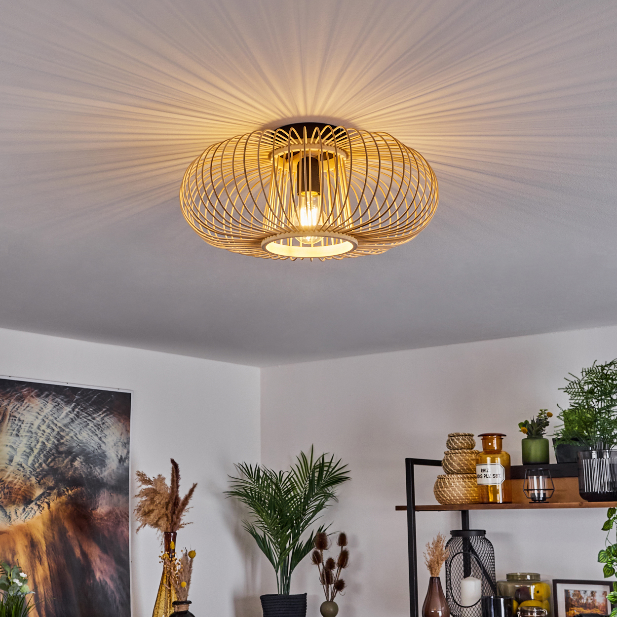 Eine dekorative Deckenlampe mit warmem Licht scheint herunter. Darunter ist ein Regal mit Pflanzen und Dekorationsartikeln zu sehen.