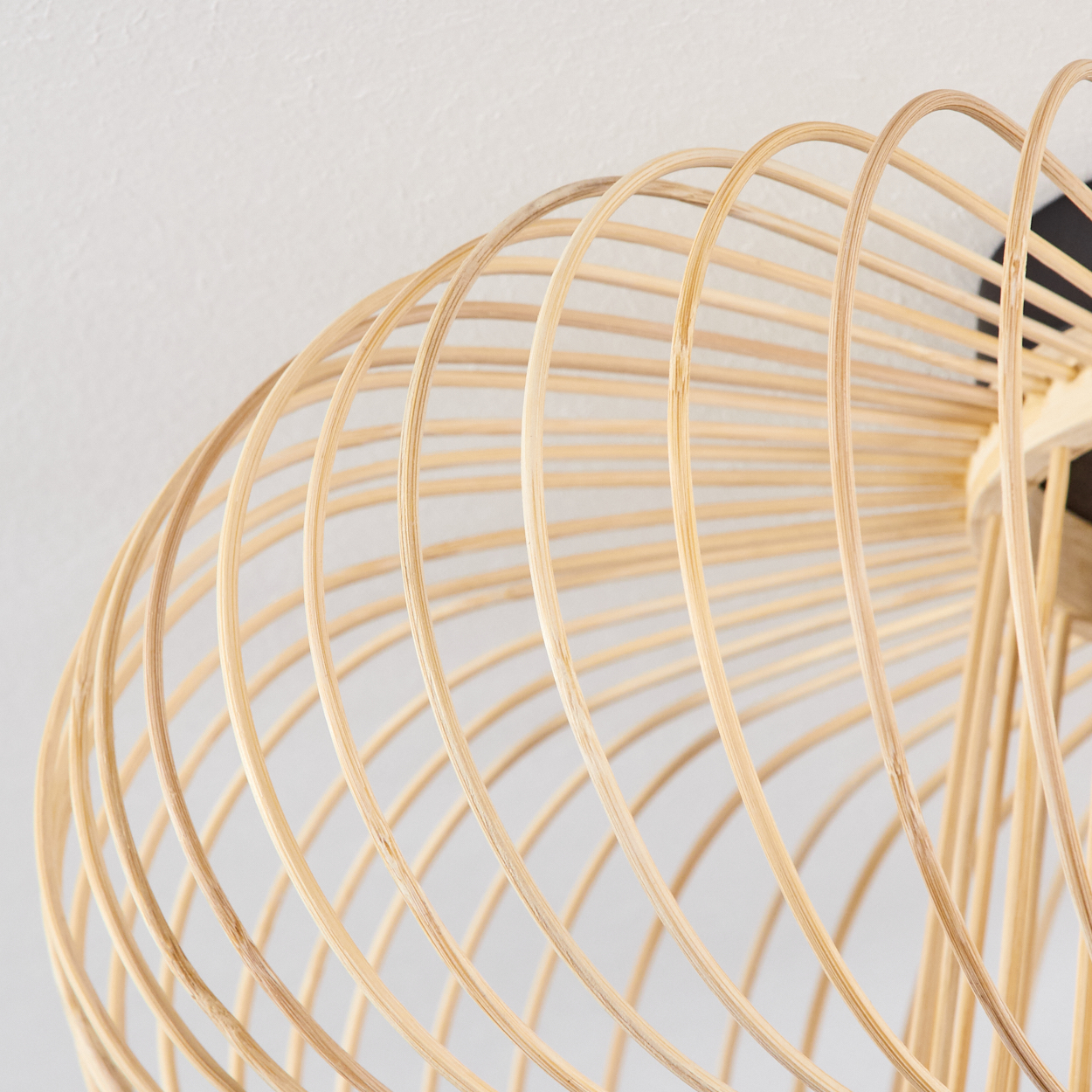 Nahaufnahme eines hellen Bambuslampenschirms vor weißem Hintergrund. Der Schirm hat ein spiralförmiges Design.