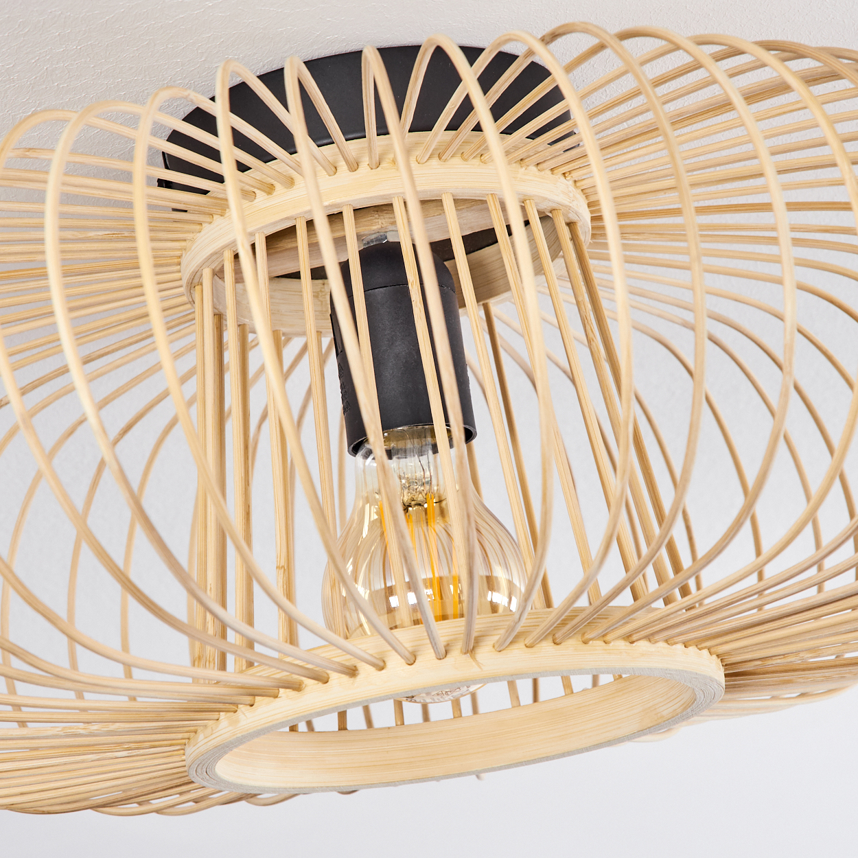 Nahaufnahme einer Deckenlampe. Sie hat einen Schirm aus gewebtem Bambus, eine schwarze Halterung und eine sichtbare Glühbirne.