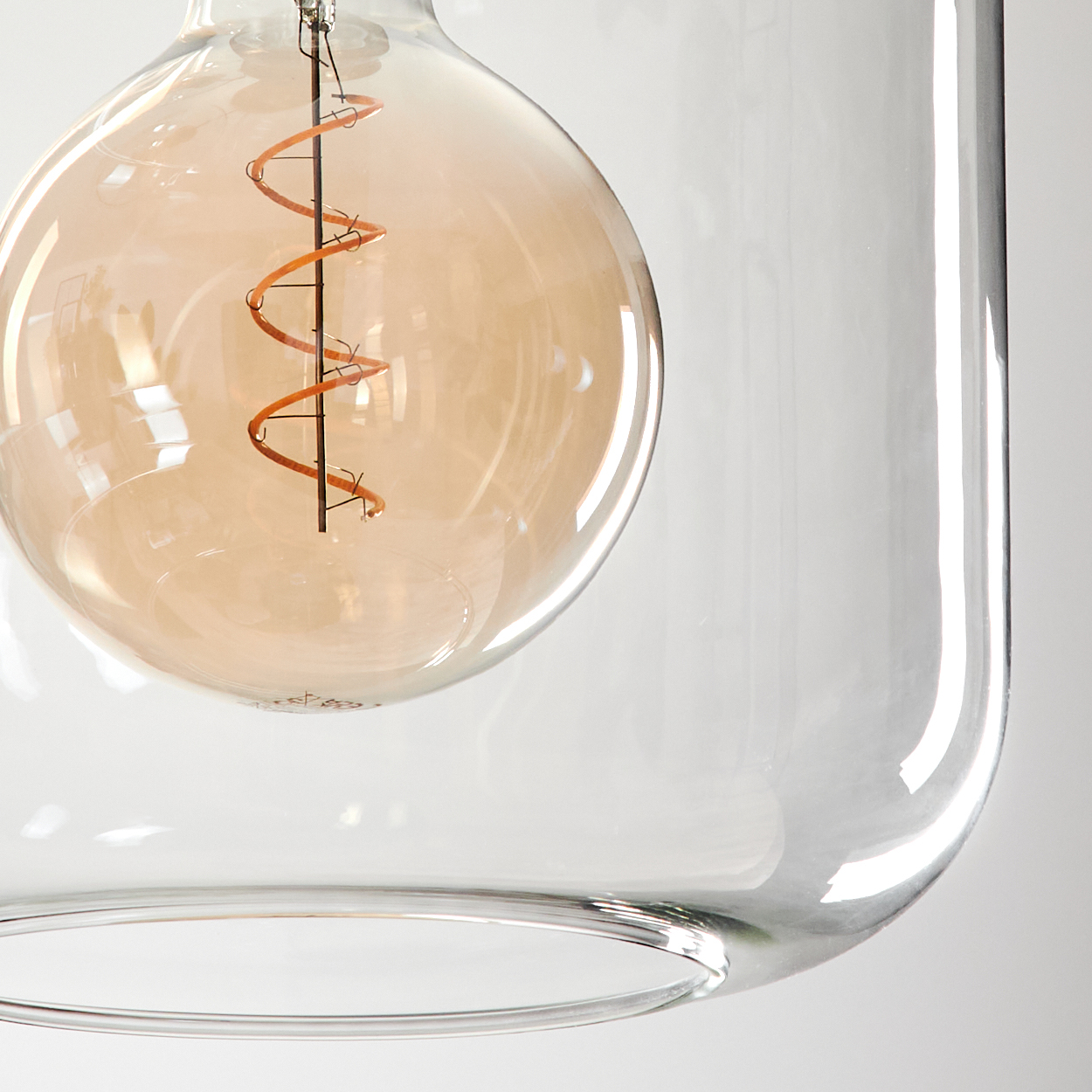 Nahaufnahme einer Glühbirne in einem Glasbehälter. Die Glühbirne ist orangefarben und hat einen Spiralfaden. Das Glas ist klar.