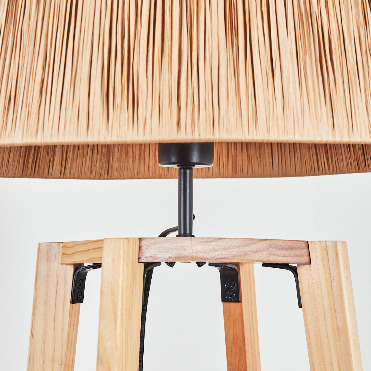 Nahaufnahme einer Lampe. Beiger gewebter Lampenschirm über einem Holzsockel mit schwarzen Metallstützen. Weißer Hintergrund.
