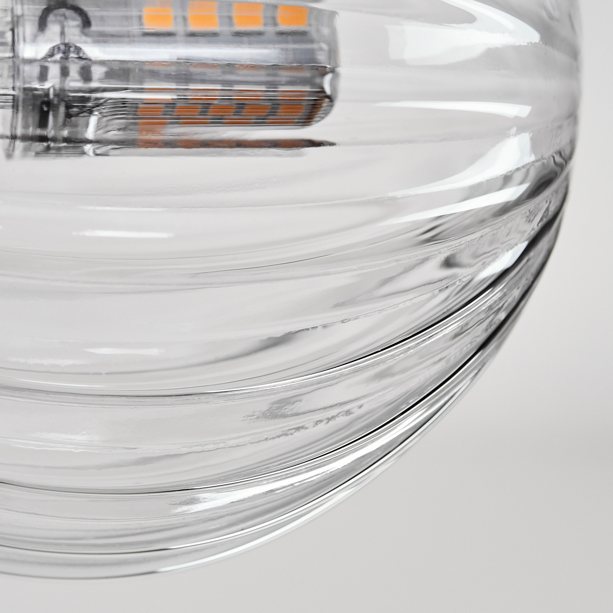Nahaufnahme einer klaren Glasleuchte mit spiralförmigem Design. Oben sind die inneren Komponenten, einschließlich orangefarbener LEDs, zu sehen.
