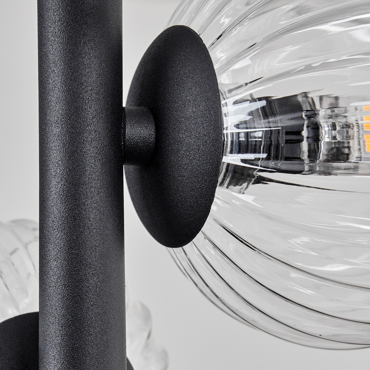Nahaufnahme einer schwarzen Metall-Lampenstange mit einer klaren, geriffelten Glaskugel. Der Hintergrund ist weiß, was die Details der Lampe hervorhebt.
