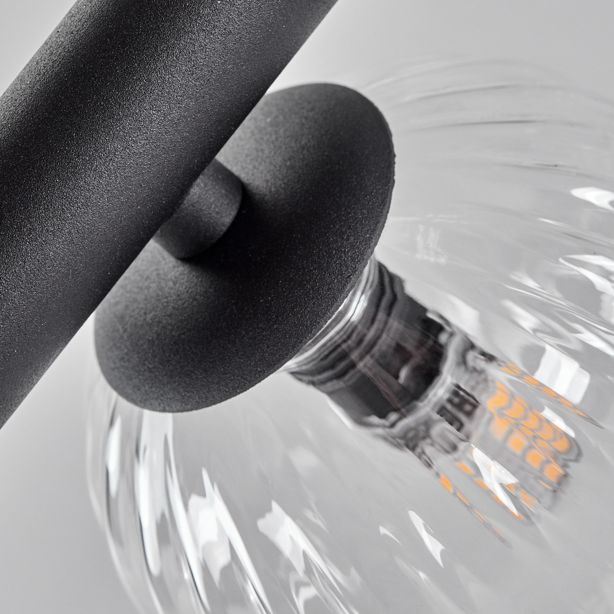 Nahaufnahme einer Leuchte mit schwarzem Metallarm, schwarzem Kugelansatz und klarer, gerippter Glühbirne mit LED.