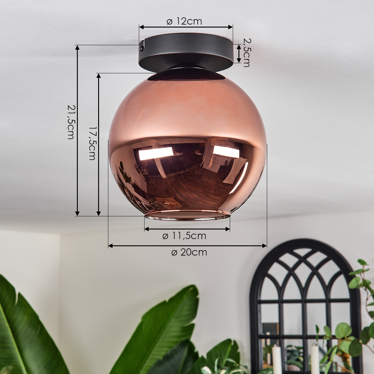 Eine kupferfarbene, kugelförmige Deckenlampe mit schwarzen Akzenten wird mit Maßlinien gezeigt. Im Hintergrund befinden sich ein schwarzes Bogenfenster und grüne Pflanzen.