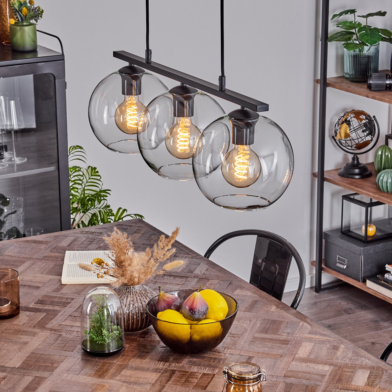 Esszimmer mit Holztisch, Obstschale, Dekorationsartikeln und Hängelampen mit sichtbaren Glühbirnen.