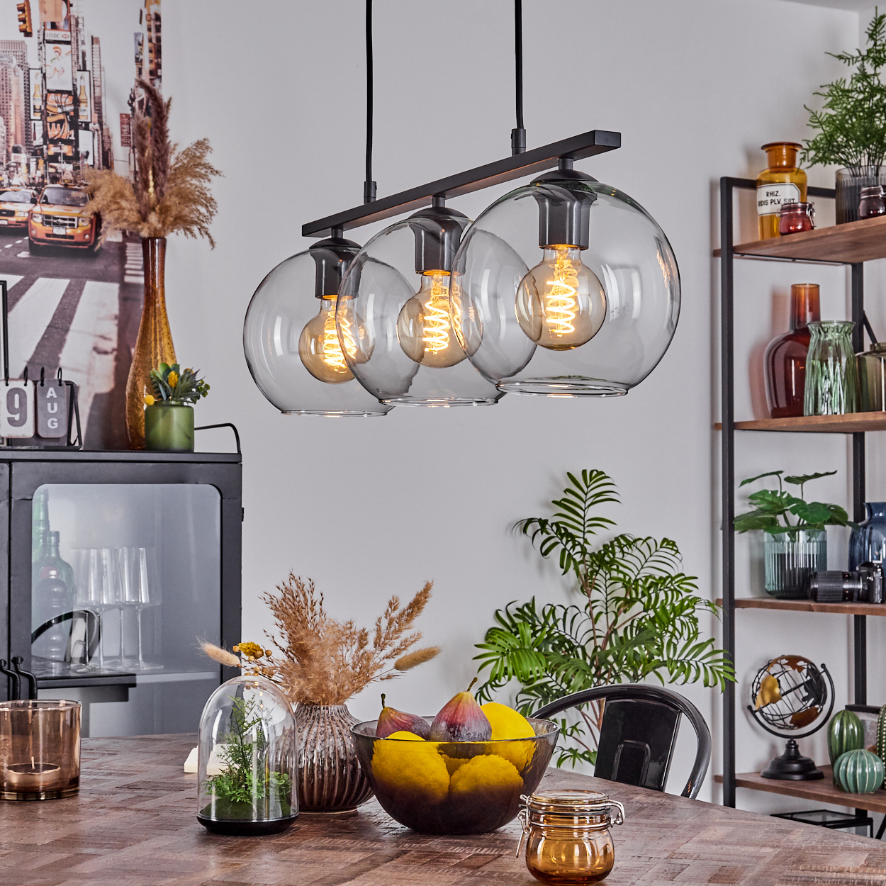 Ein Esszimmer mit Holztisch, moderner Kronleuchter mit drei Glaskugeln und verschiedene Dekorationsartikel.