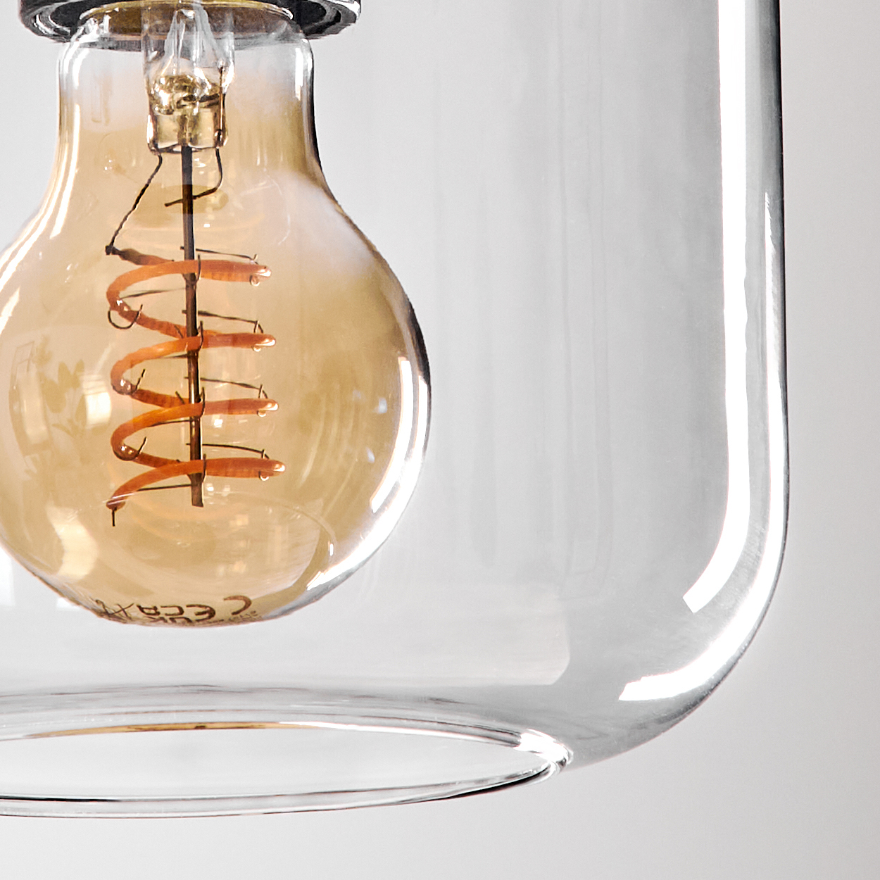 Nahaufnahme einer Glühbirne in einem gläsernen Lampenschirm. Die Glühbirne hat einen Spiralglühfaden, und das Glas ist klar.