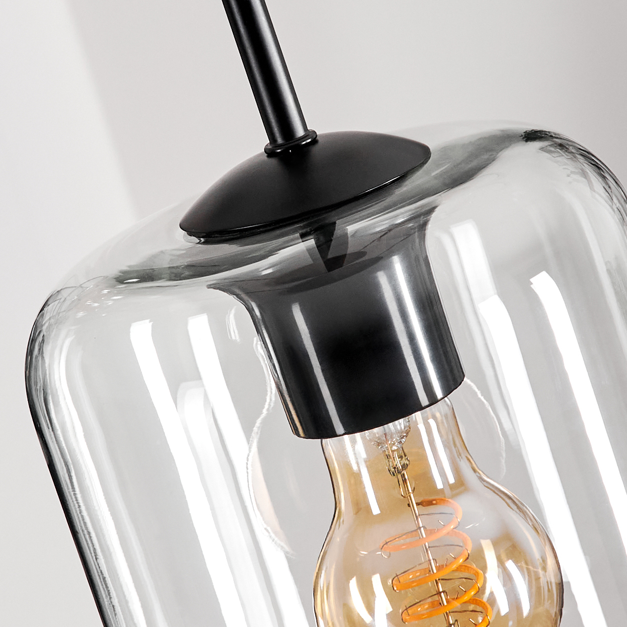 Nahaufnahme einer Glaslampe. Die Lampe hat einen schwarzen Deckel und einen klaren Glasschirm mit einer sichtbaren Glühbirne.
