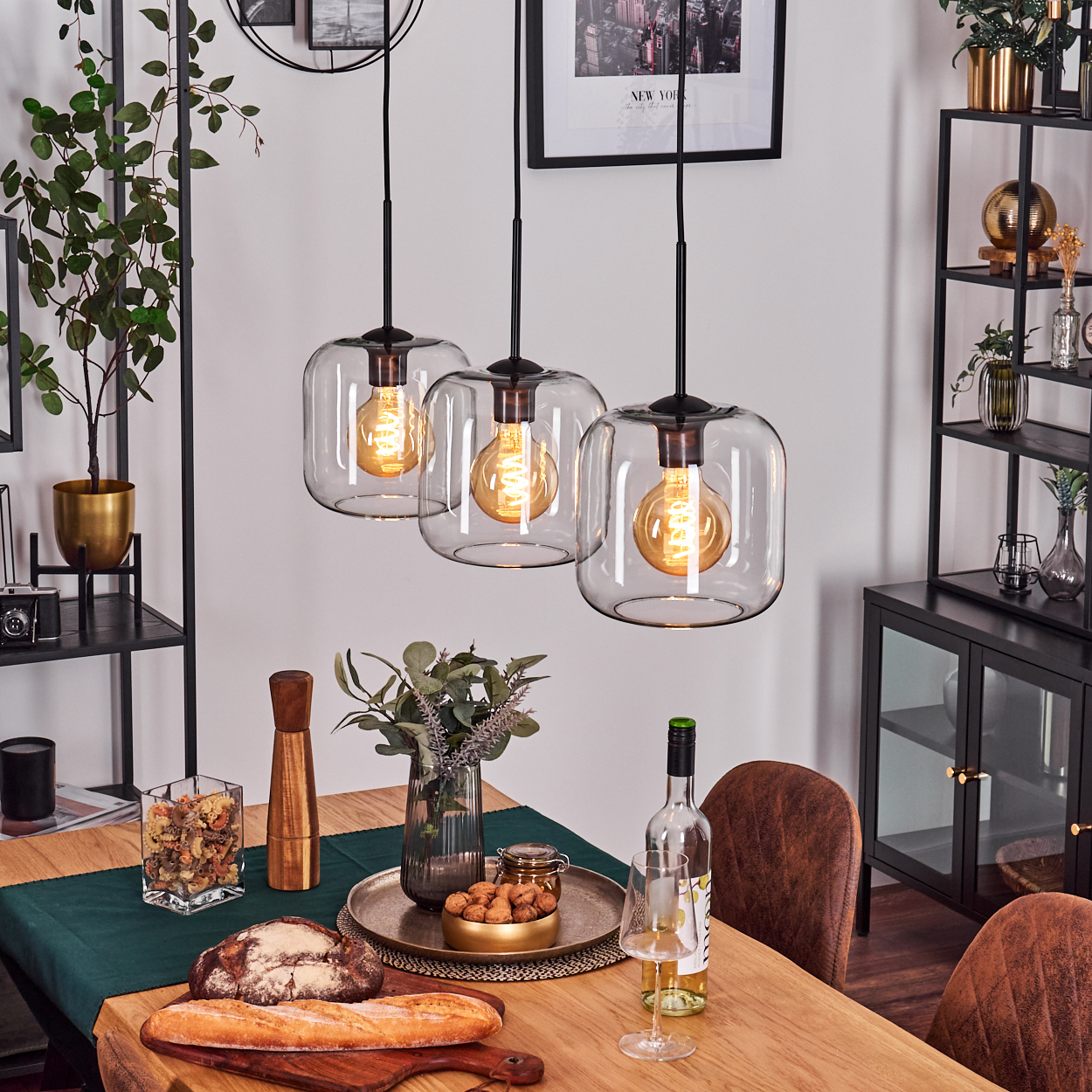 Esstisch mit Hängelampen, Essen, Wein und Stühlen. Der Hintergrund umfasst Regale mit Dekor und gerahmten Bildern.