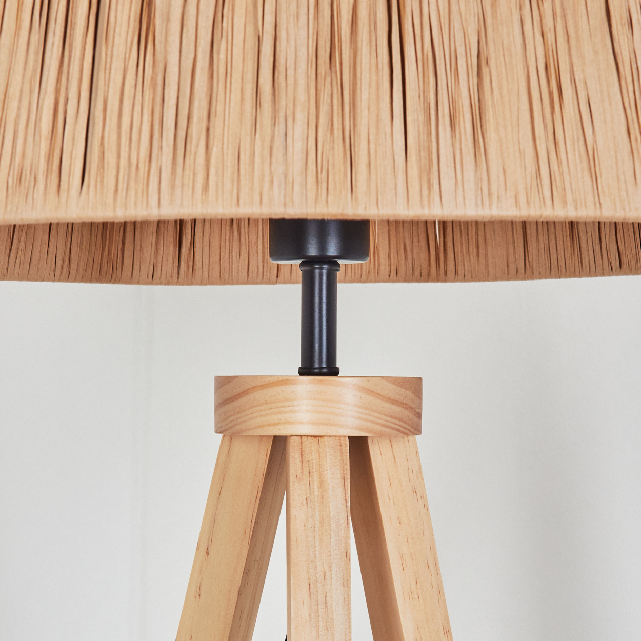 Nahaufnahme einer Lampe. Sie hat einen hellbraunen Lampenschirm, schwarzen Ständer und einen Holzsockel. Der Hintergrund ist weiß.