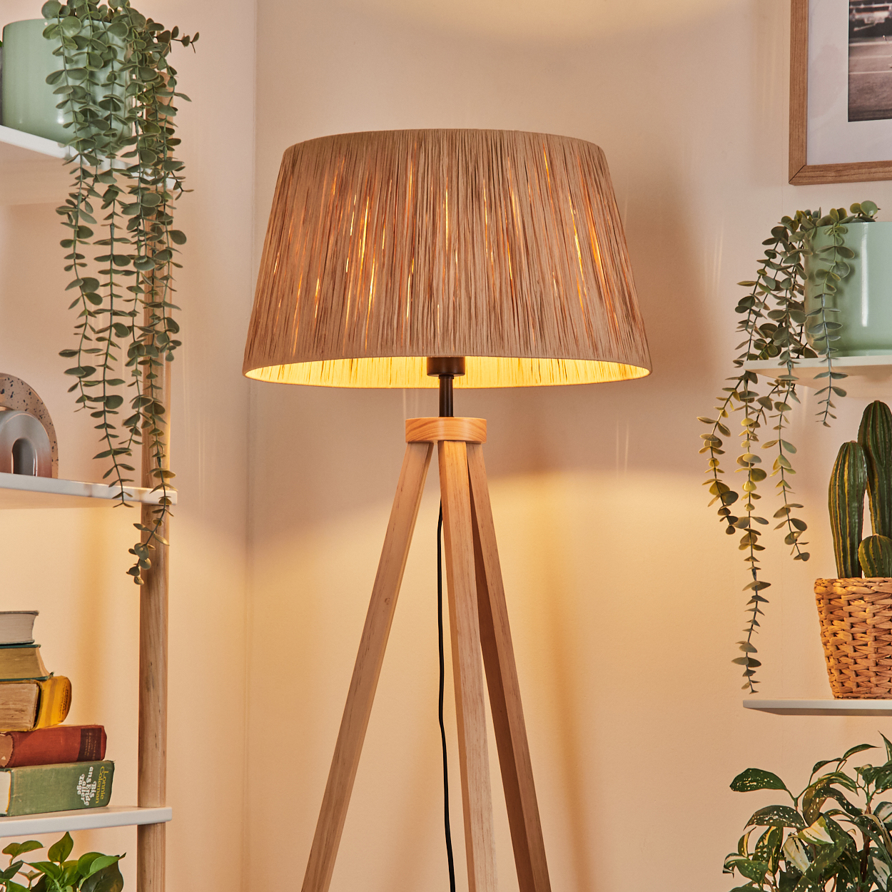 Eine Holz-Stativlampe mit beigem Lampenschirm. Regale mit Pflanzen und Büchern befinden sich auf beiden Seiten. Ein warmes, einladendes Interieur.