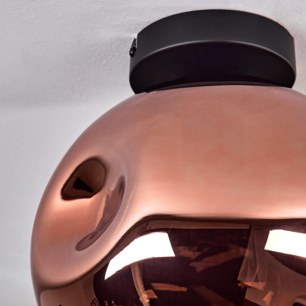 Eine moderne Deckenlampe mit kupferfarbenem Schirm und schwarzem Sockel. Die Lampe ist an einer weißen Decke montiert.