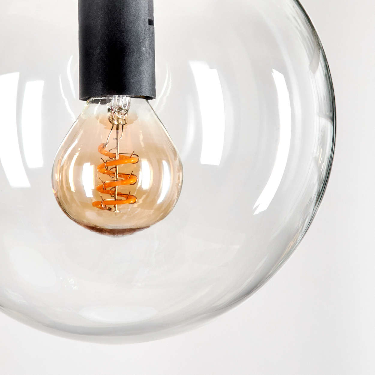 Eine klare Glaskugel-Pendelleuchte mit einer warm getönten Glühbirne. Die Glühbirne hat einen orangefarbenen Wendelfaden, die Halterung ist schwarz.