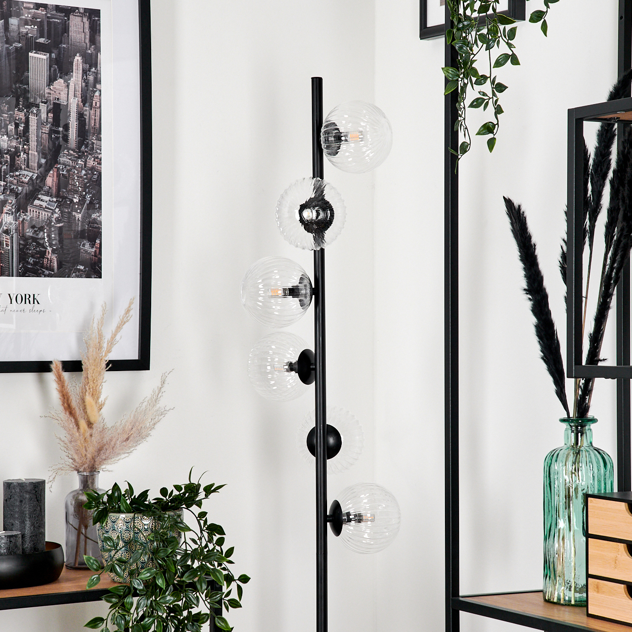 Eine moderne Stehlampe mit Glaskugelschirmen, gerahmter Kunst und Dekorationsartikeln auf einem Regal vor einer weißen Wand.