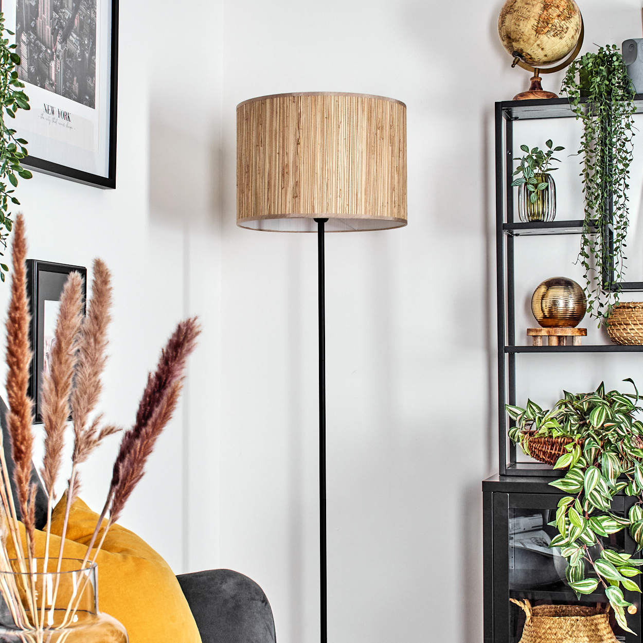 Ein Raum mit Stehlampe, Regalen mit Pflanzen und Dekoration sowie einem gerahmten New York-Bild. Im Vordergrund ein Sofa mit gelben Kissen.