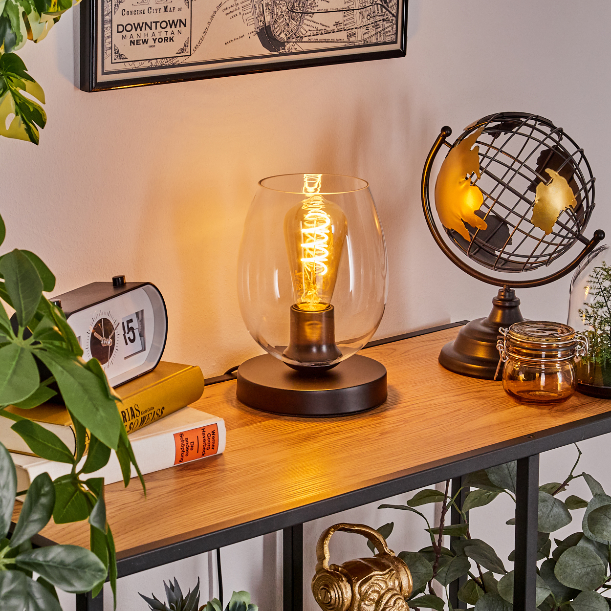 Eine Lampe steht auf einem Holzregal mit Globus, Uhr und Büchern. Im Hintergrund hängt eine Karte. Pflanzen befinden sich auf und um das Regal.