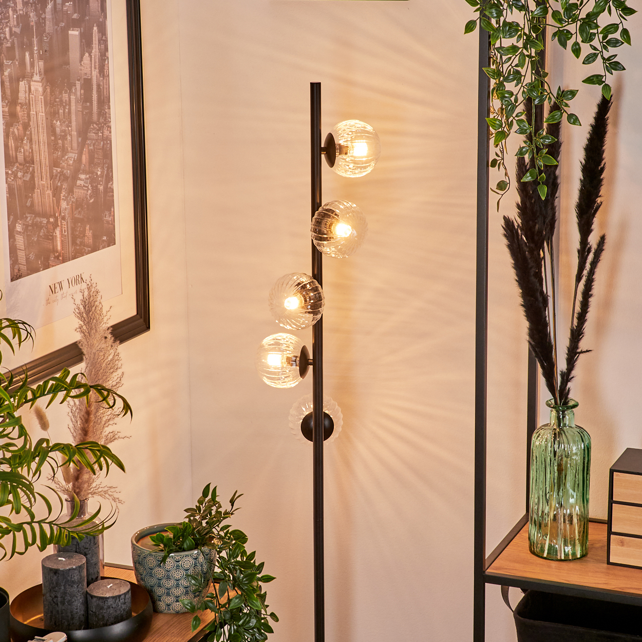 Eine Stehlampe mit vier Glaskugelleuchten steht in der Nähe von Pflanzen und einem gerahmten Poster der Skyline von New York City.