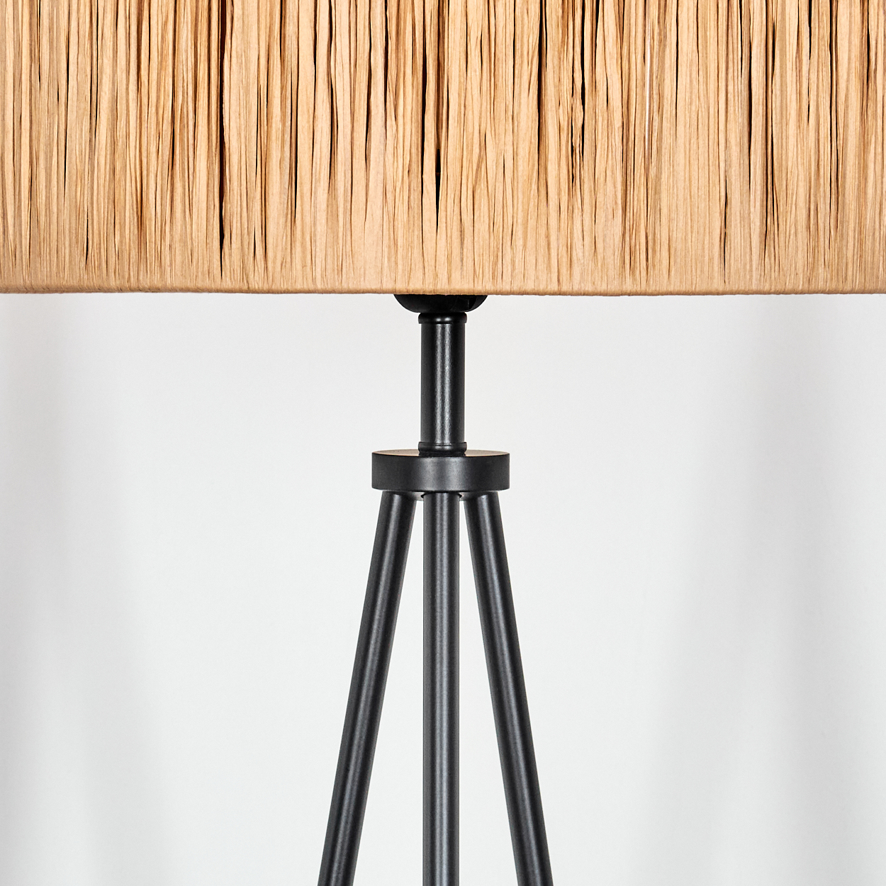 Nahaufnahme einer Lampe. Der Lampenschirm ist beige, zylindrisch, und der Sockel ist schwarz mit Stativdesign. Der Hintergrund ist weiß.