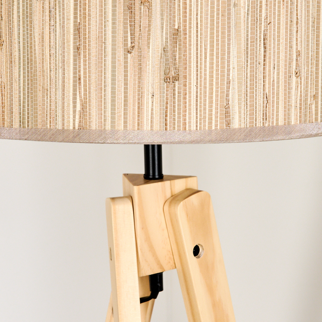 Nahaufnahme einer hölzernen Stativlampe. Der Lampenschirm besteht aus geflochtenem Stroh. Der Lampenständer ist helles Holz mit einer schwarzen Metallstange.