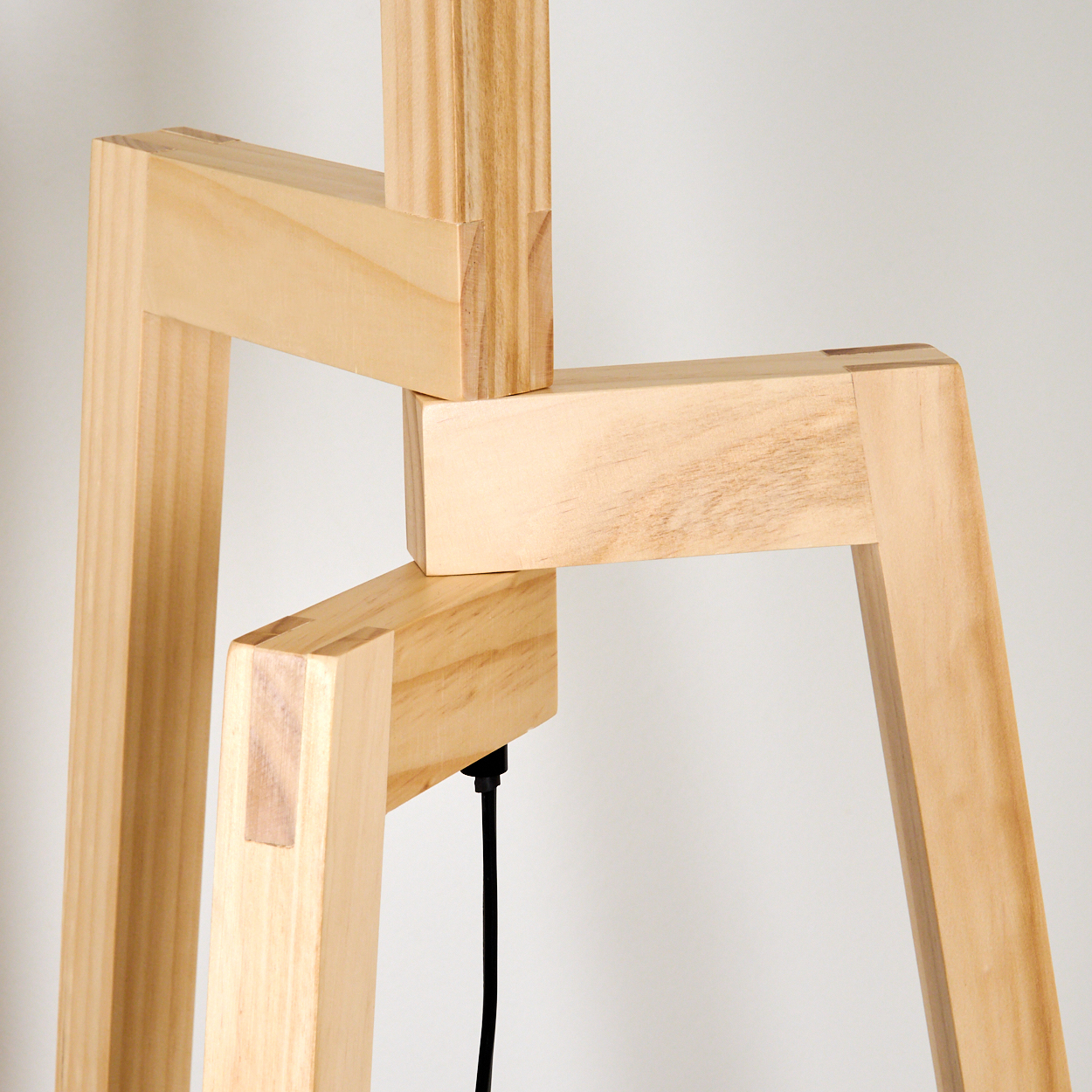 Holzlampengestell mit ineinandergreifenden Verbindungen. Naturholzfarbe. Ein schwarzes Kabel hängt herunter. Weißer Hintergrund.
