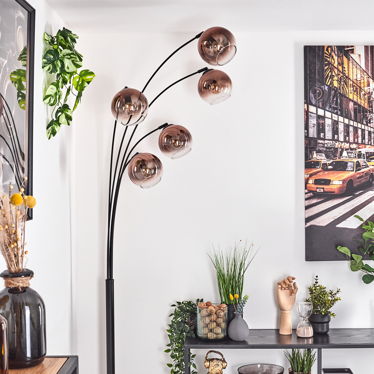 Ein modernes Wohnzimmer mit einer schwarzen Stehlampe mit fünf kugelförmigen Lichtern. Auf einem schwarzen Regal befinden sich Dekorationsartikel.